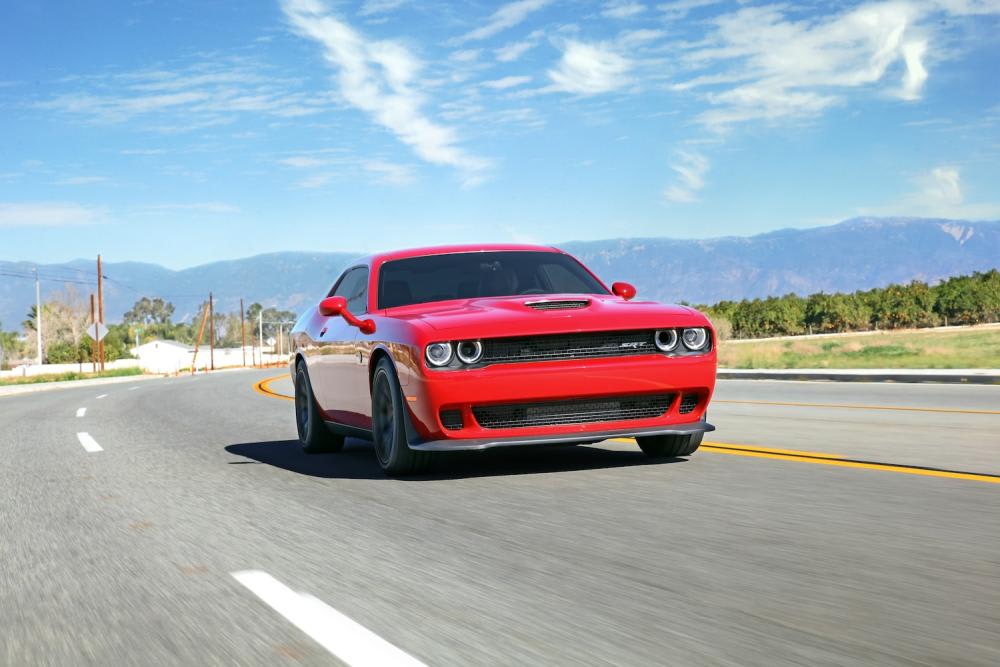 Curved 4 lane road with with bright red Dodge Challenger SRT powering through the curve as a lush green treeline lines both sides of the road with the San Bernardino Mountains standing proud in the background under a blue sky with very few clouds present